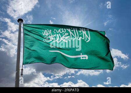 Flagge Saudi-Arabiens, nationales Symbol des Königreichs Saudi-Arabien auf einem Fahnenmast, der gegen den blau bewölkten Himmel winkt Stockfoto