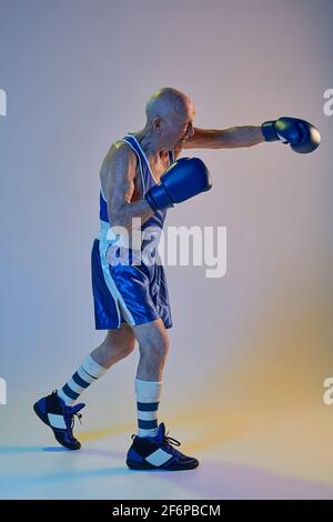 Senior Mann trägt Sportkleidung Boxen isoliert auf Gradienten Studio Hintergrund in Neonlicht. Konzept von Sport, Aktivität, Bewegung, Wohlbefinden. Copyspace Stockfoto