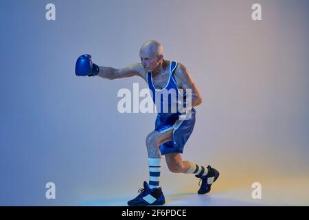 Senior Mann trägt Sportkleidung Boxen isoliert auf Gradienten Studio Hintergrund in Neonlicht. Konzept von Sport, Aktivität, Bewegung, Wohlbefinden. Copyspace Stockfoto