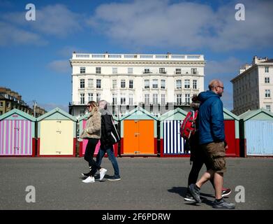 Die Menschen laufen an Strandhütten entlang der Promenade neben Brighton Beach, East Sussex. Bilddatum: Freitag, 2. April 2021. Stockfoto