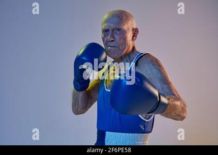 Senior Mann trägt Sportkleidung Boxen isoliert auf Gradienten Studio Hintergrund in Neonlicht. Konzept von Sport, Aktivität, Bewegung, Wohlbefinden. Copyspace Stockfoto