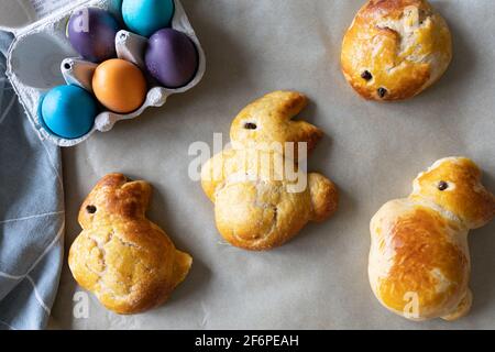 Süßer Brioche-Teig in Form von Osterhasen und einem Eierkarton mit farbigen Ostereiern. Stockfoto