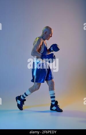 Senior Mann trägt Sportkleidung Boxen isoliert auf Gradienten Studio Hintergrund in Neonlicht. Konzept von Sport, Aktivität, Bewegung, Wohlbefinden. Copyspace Stockfoto