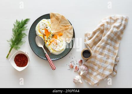 Schale mit Türkischen Cilbir Eier, Joghurt, pochierte Eier, Knoblauch, Chili, frischer Dill und zerlassener Butter. Verziert mit wenigen Stücke von lavash Brot ein Stockfoto