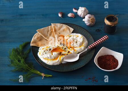 Schale mit Türkischen Cilbir Eier, Joghurt, pochierte Eier, Knoblauch, Chili, frischer Dill und zerlassener Butter. Verziert mit wenigen Stücke von lavash Brot ein Stockfoto