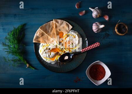 Schale mit Türkischen Cilbir Eier, Joghurt, pochierte Eier, Knoblauch, Chili, frischer Dill und zerlassener Butter. Verziert mit wenigen Stücke von lavash Brot ein Stockfoto