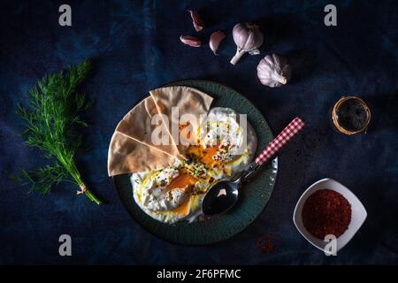 Schale mit Türkischen Cilbir Eier, Joghurt, pochierte Eier, Knoblauch, Chili, frischer Dill und zerlassener Butter. Verziert mit wenigen Stücke von lavash Brot ein Stockfoto