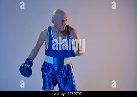 Senior Mann trägt Sportkleidung Boxen isoliert auf Gradienten Studio Hintergrund in Neonlicht. Konzept von Sport, Aktivität, Bewegung, Wohlbefinden. Copyspace Stockfoto