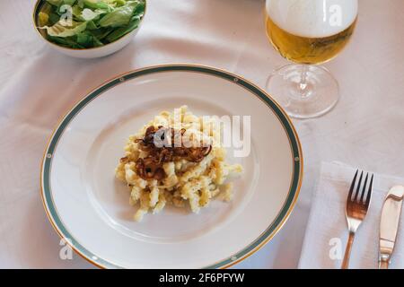 Tiroler Käsekuchen Noodles oder Pasta Kaesespätzle mit gebratenen Zwiebeln auf einem weißen Teller, ein typisches und traditionelles österreichisches Gericht serviert mit grünem Sala Stockfoto