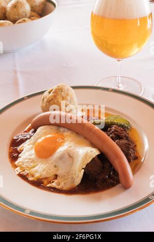 Fiakergulasch oder Herrengulasch Wiener Rindergulasch garniert mit einem Brotknödel, Frankfurter Wurst, gebratenen Ei und Gherkin auf einem Teller, serviert mit Stockfoto