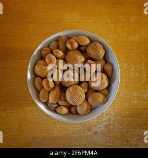 Weiße Schale mit ungeschalten Nüssen auf einem abgenutzten Holztisch, von oben gesehen. Stockfoto