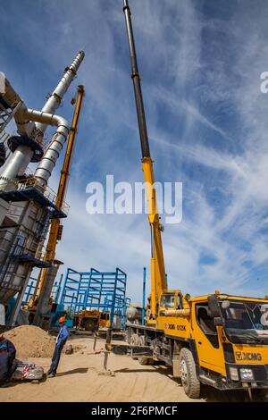 Aktau, Kasachstan - 19. Mai 2012: Bau einer asphaltischen Bitumenfabrik Raffineriesäule. Grauer Destillationsturm, Arbeiter und gelber Mobilkran (h Stockfoto