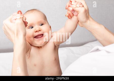 Physiotherapeut, der Sit-up-Übungen mit einem sechsmonatigen Mädchen in der Kinderklinik durchführt. Arzt zieht Säugling in sitzende Position, um zu stärken Stockfoto