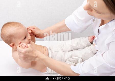 Physiotherapeut, der Sit-up-Übungen mit einem sechsmonatigen Mädchen in der Kinderklinik durchführt. Arzt zieht Säugling in sitzende Position, um zu stärken Stockfoto