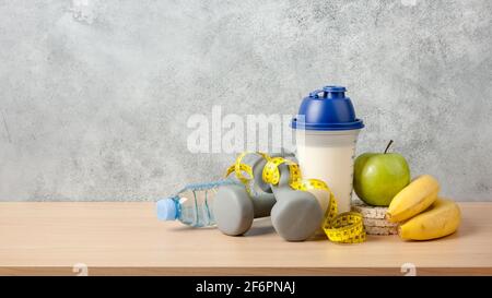 Proteincocktail, Kurzhanteln, Maßband, Wasserflasche und frisches Obst auf Holztisch Stockfoto