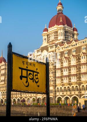 Mumbai, Indien - 7. März 2021 : Mumbai-Schild in Marathi-Sprache mit Heritage Grand Class fünf-Sterne-Hotel Taj, neben dem Gateway of India. Stockfoto