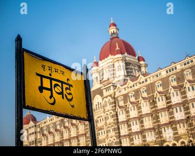 Mumbai, Indien - 7. März 2021 : Mumbai-Schild in Marathi-Sprache mit Heritage Grand Class fünf-Sterne-Hotel Taj, neben dem Gateway of India. Stockfoto