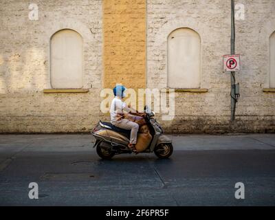 Mumbai, Indien - 7. Januar 2021 : Unidentifizierter Mann mit Covid-Maske auf den Straßen von Mumbai, der mit Gepäck auf einem Roller unterwegs ist Stockfoto