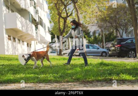 10. März 2021 - Faro, Portugal: Frau mit Gesichtsmaske läuft mit ihrem Hund vor der Wohnanlage Stockfoto