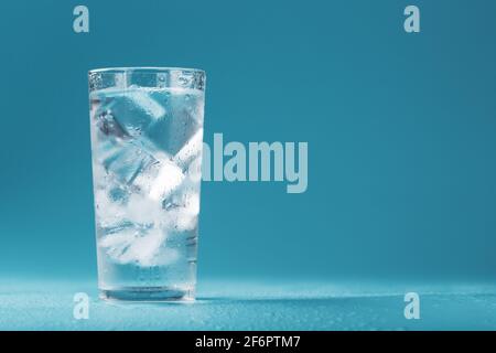 Eiswürfel in einem vernebelten Glas mit Tropfen Eiswasser Nahaufnahme Makro. Erfrischendes und kühlendes Getränk bei heißem Wetter. Blauer Hintergrund. Vollbild Stockfoto