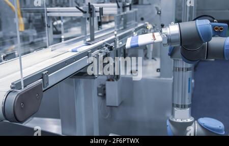 Automatisierter Roboterarm lädt Kosmetikschlauch aus Aluminium zur Füllmaschine In der Produktionslinie Stockfoto