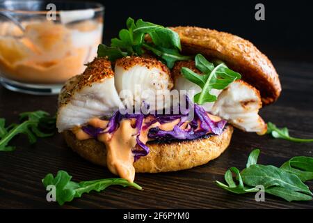 Brockened Fish Burger und Sriracha Mayo: Ein Fischsandwich aus Heilbutt mit Rotkohl und Rucola auf einem Vollkornbrötchen Stockfoto