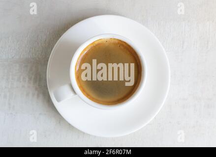 Duftender Espresso in einer weißen Tasse und Untertasse. Morgendliche Tradition. Konzept für die Zubereitung von Hauskaffee. Horizontale Ausrichtung. Draufsicht. Stockfoto