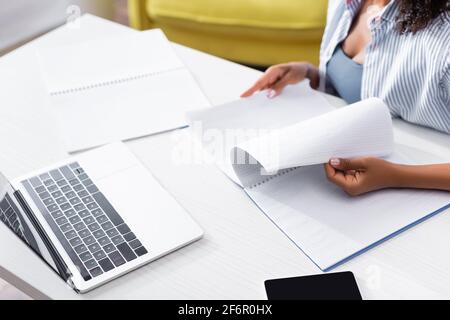 Beschnittene Ansicht einer afroamerikanischen Frau, die Notebook in der Nähe von Gadgets hält Stockfoto