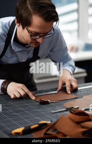 Geschickter Arbeiter der Lederherstellung, der einige Proben schneidet. Stockfoto