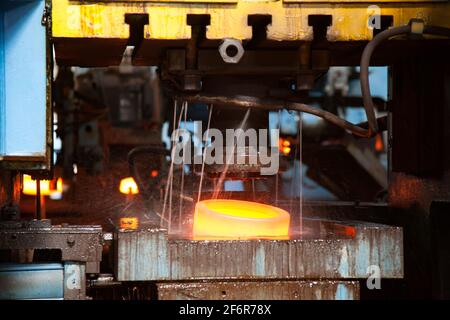 Lageranlage. Stanzen des Lageraußenrings an der mechanischen Presse. Wasserkühlung des rotheißen Metalls. Nahaufnahme des Fotos. Geringe Schärfentiefe.Scharfstellung Stockfoto