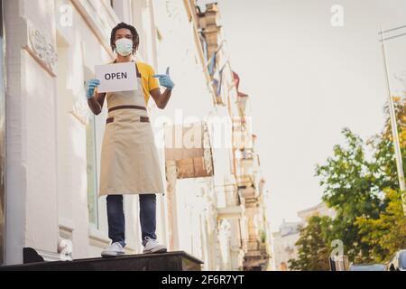 Ganzkörperfoto mit dem Kellner, der die Schürze trägt Ein offener Tisch lädt die Gäste während des Restaurants in Gesichtsmaske ein Sperre Stockfoto