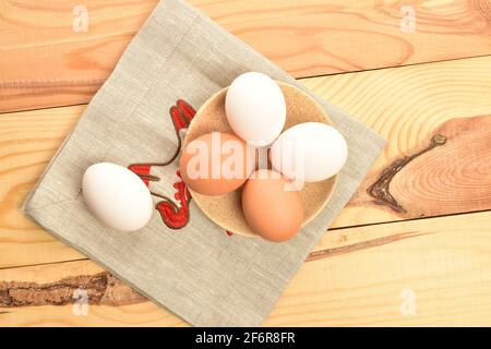 Vier frische, leckere, weiße und beige Hühnereier aus biologischem Anbau in einer hellen Keramikuntertasse auf einer Leinenserviette. In der Nähe, auf einer Leinenserviette. Stockfoto