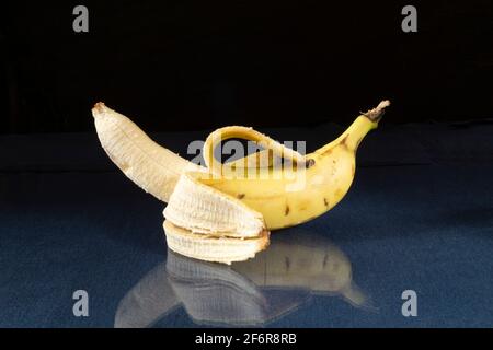 Eine reife Banane auf einem Glastisch mit Spiegelung. Essen auf schwarzem Hintergrund Stockfoto