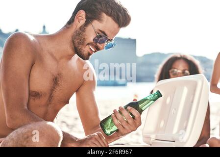 Genießen Sie unbeschwerte Zeit mit Freunden. Fröhlicher junger Menschen verbringen eine schöne Zeit zusammen, während am Strand zu sitzen und Bier trinken. Stockfoto