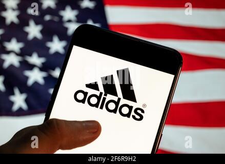 In dieser Abbildung ist das Logo der deutschen multinationalen Sportbekleidungsmarke Adidas auf einem Android-Mobilgerät mit Flagge der Vereinigten Staaten von Amerika (USA), allgemein bekannt als die Vereinigten Staaten (USA oder USA), im Hintergrund zu sehen. (Foto von Budrul Chukrut / SOPA Images/Sipa USA) Stockfoto