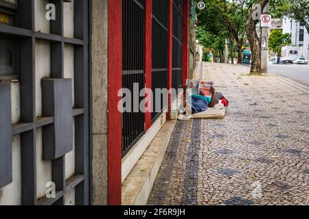 Brasilianischer Obdachloser, DER AUF einer Matratze auf dem Bürgersteig einer Straße in Belo Horizonte, Brasilien, liegt. Er liest eine Zeitung. Stockfoto