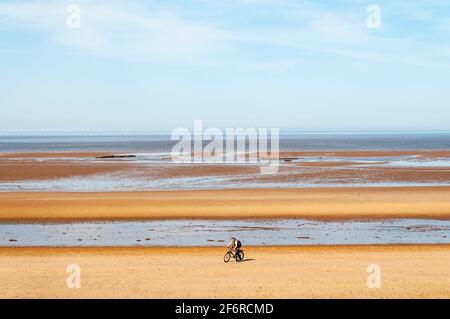 Ein Mann, der mit dem Fahrrad an einem ansonsten menschenleeren Strand bei Holme-next-the-Sea an der Nord-Norfolk-Küste entlang fährt. Stockfoto