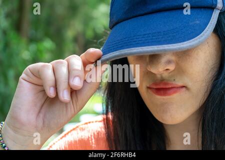 Frau versteckt ihr Gesicht hinter einer blauen Basecap Stockfoto