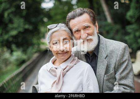 Schönes kaukasisches Seniorenpaar in stilvoller Kleidung, das im grünen Park umarmt spazieren geht. Glückliche Frau und Ehemann verbringen Zeit zusammen an der frischen Luft. Stockfoto