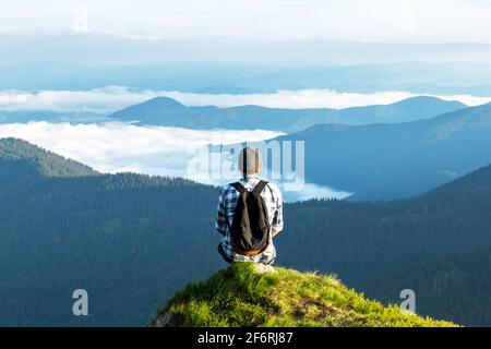 Ein Tourist sitzt am Rande einer Klippe mit einem rosa Teppich von Rhododendron Blumen im Sommer bedeckt. Neblige Berge im Hintergrund. Querformat p Stockfoto