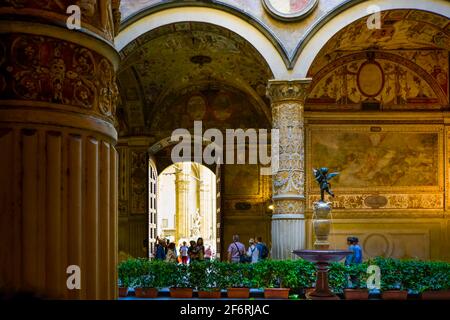 Einheimische und Touristen besuchen den ersten Innenhof des Palazzo Vecchio in Florenz Italien mit einem kleinen Brunnen mit Statue, Fresken und gewölbten Säulen Stockfoto