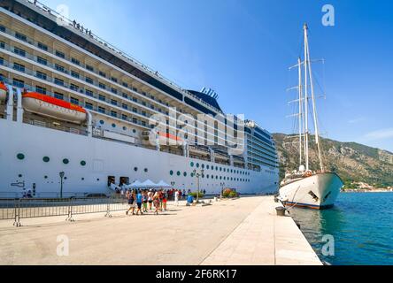 Touristen stehen neben einem massiven Kreuzfahrtschiff am Kreuzfahrthafen der Bucht von Kotor, Montenegro. Stockfoto