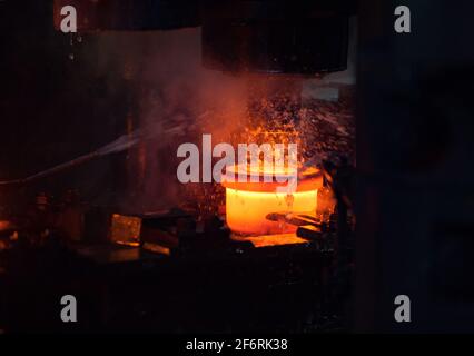 Lageranlage. Stanzen des Innenrings des Lagers auf einer mechanischen Presse. Wasserkühlung des Metalls. Rot-heißes Metall. Nahaufnahme des Fotos Stockfoto