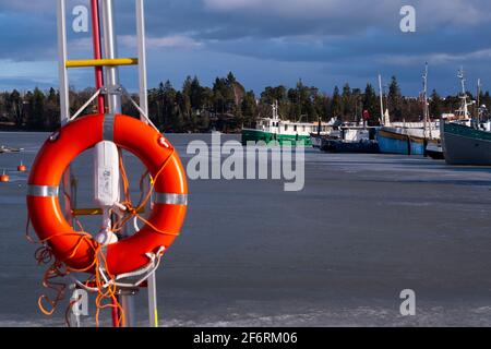 Helsinki / Finnland - 2. APRIL 2021: Eine Frühlingsszene eines kleinen Freizeitboothafens mit orangefarbenem Lebensretter im Vordergrund. Stockfoto