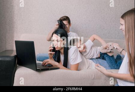 Aktive Kinder frönen, stören und ablenken ihre Mutter, während sie zu Hause auf einem Laptop arbeiten Stockfoto