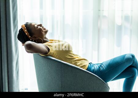 Lächelnde afroamerikanische Frau, die sich in einem Schaukelstuhl ausruht, ein zufriedenes Mädchen, das sich zu Hause im gemütlichen Stuhl ausruht, ein faules Wochenende verbringt, träumt Stockfoto