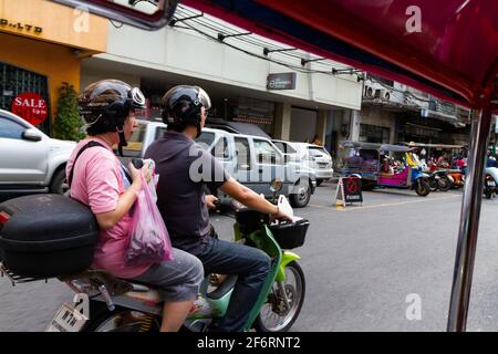 Bangkok, Thailand - 16. Juli 2016: Eine Frau hält ihre Lebensmittel auf dem Rücken eines fahrenden Rollers fest. Stockfoto