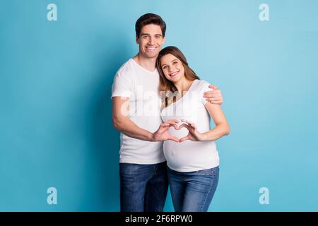 Foto-Porträt von zwei Menschen glückliches Paar Ehemann schwanger Frau Zeigt die Finger des Herzsymbols in einem leuchtenden blauen Hintergrund Stockfoto
