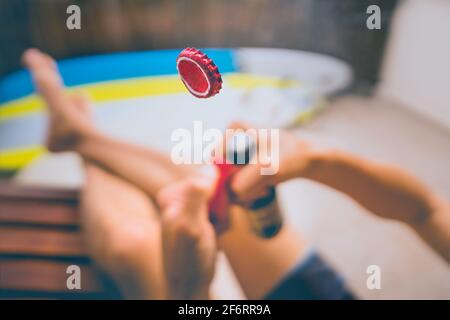 Öffnen einer Flasche Bier mit Feuerzeug. Konzentrieren Sie sich auf die Kappe in der Luft. Kaltes Bier trinken und sonniges Sommerwochenende genießen Stockfoto