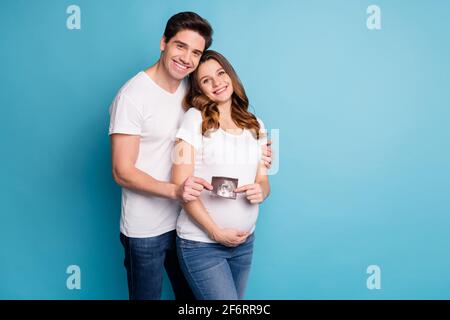 Foto von jungen fröhlich positiv lächelnd glücklich Familie halten Ultraschall Foto von Baby isoliert auf blauem Hintergrund Stockfoto